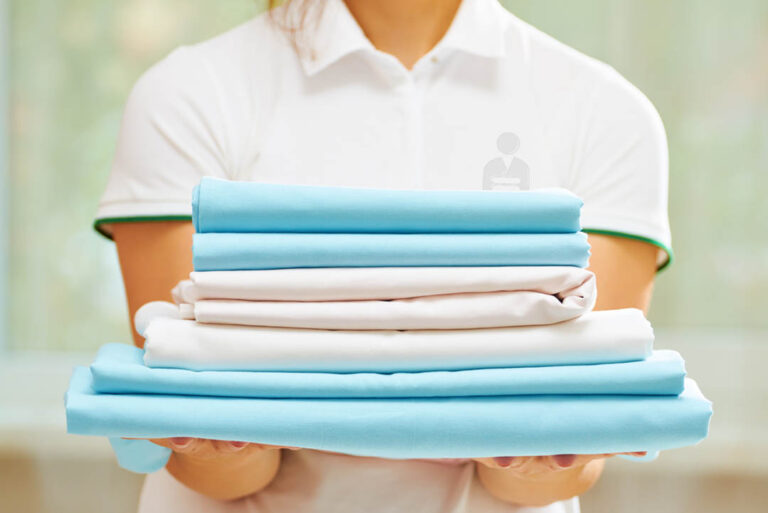 Servizi closeup of woman's hand holding a stack of clean folded bed sheets of blue and white colors. blurred background.